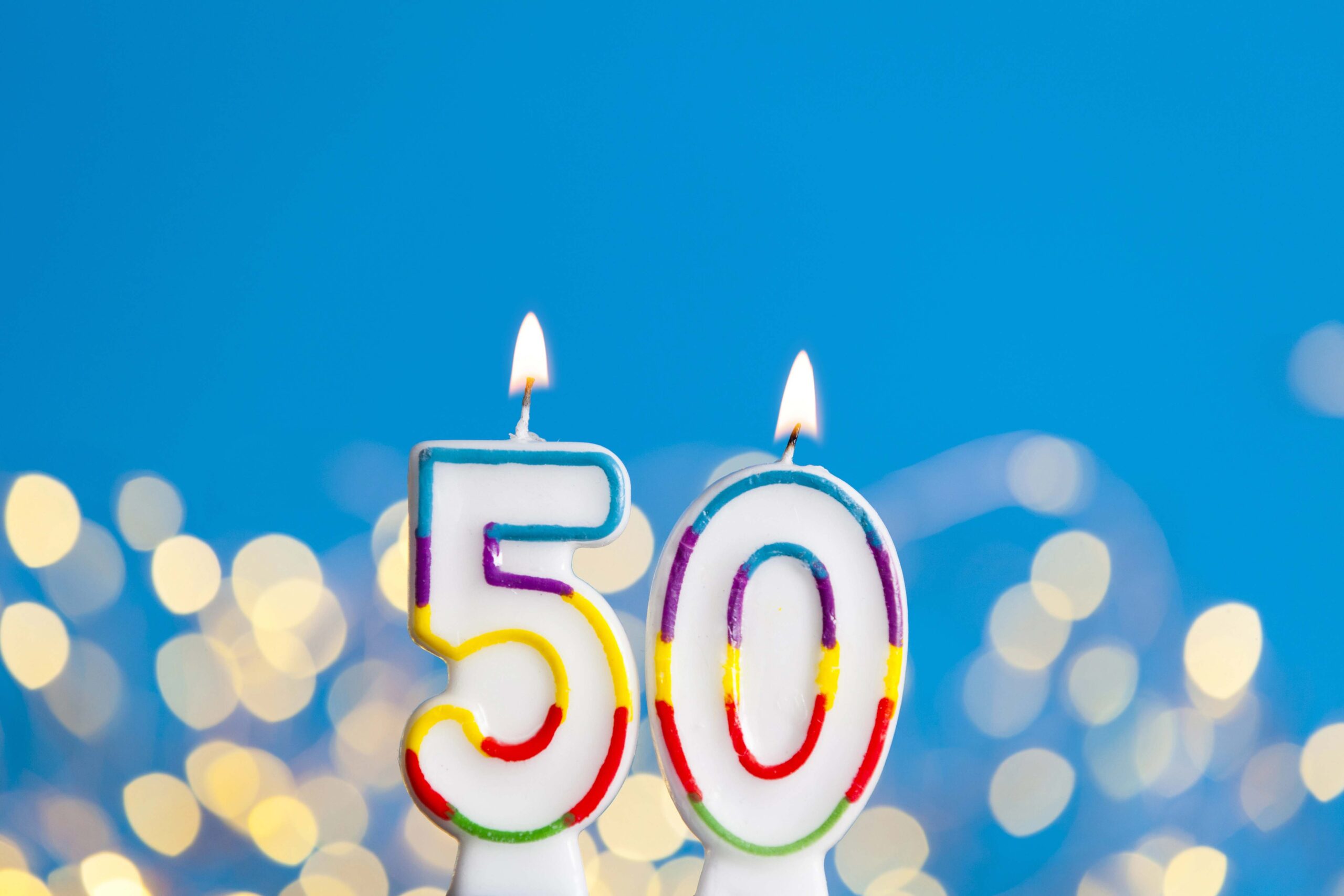 Number 50 birthday celebration candle against a bright lights and blue background